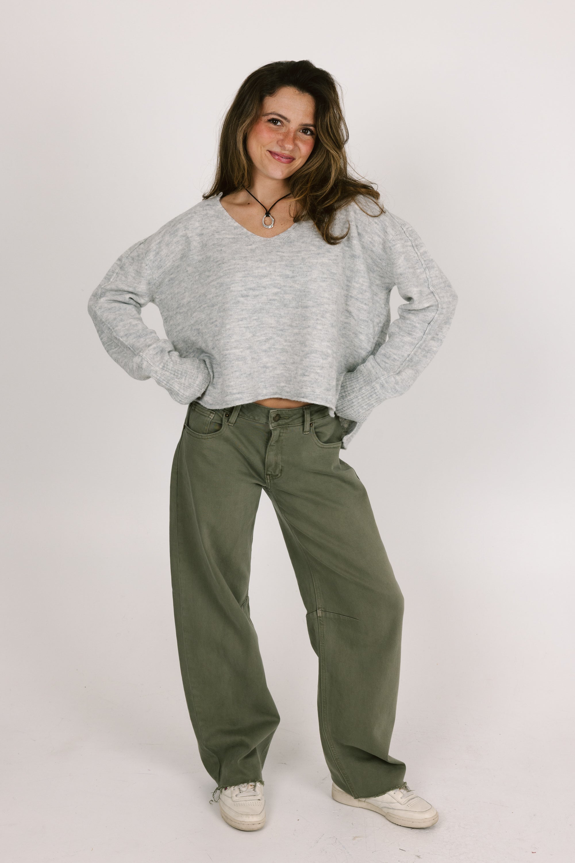 Woman wearing a gray sweater and green pants on a white background