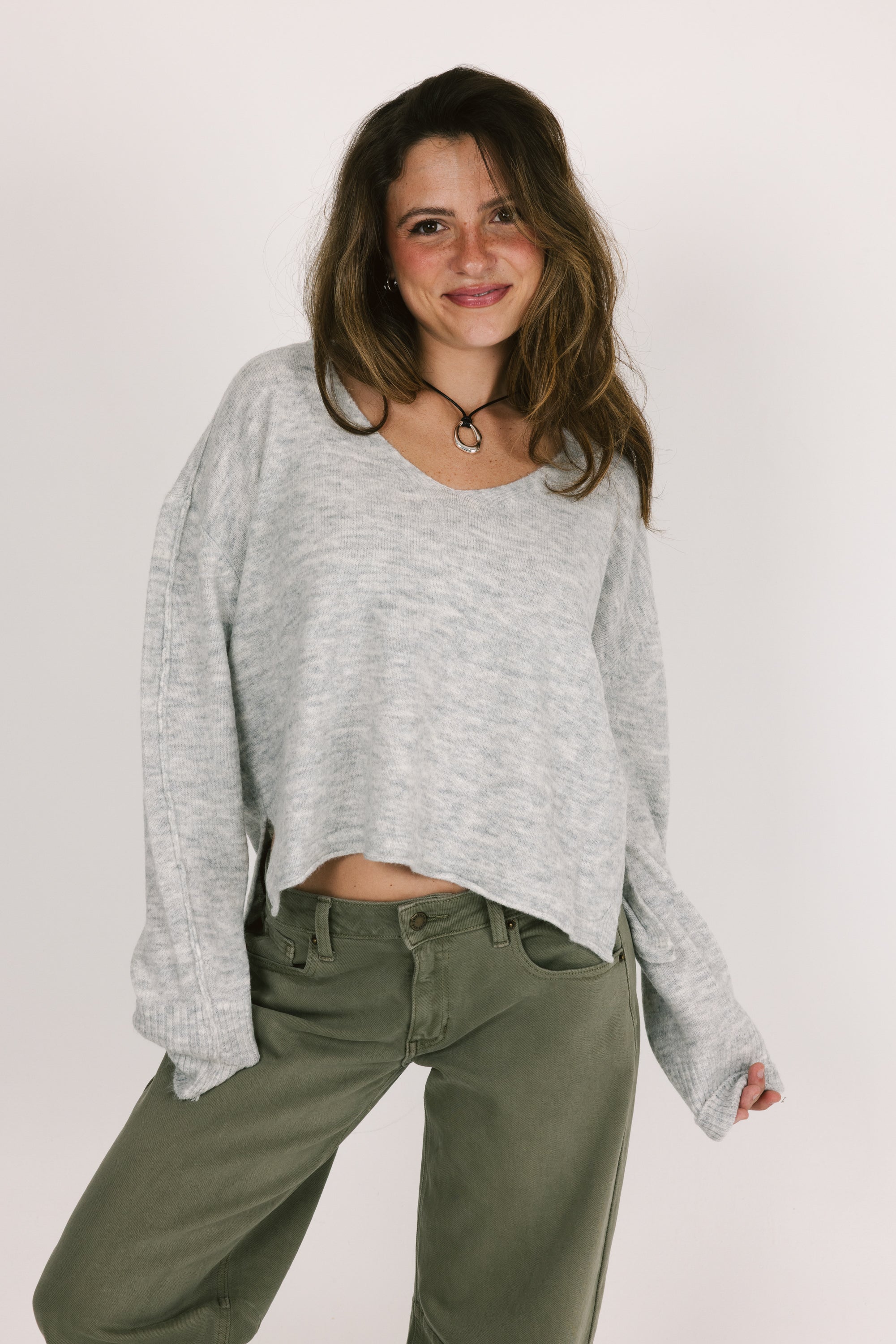 Woman wearing a gray sweater and green pants against a white background
