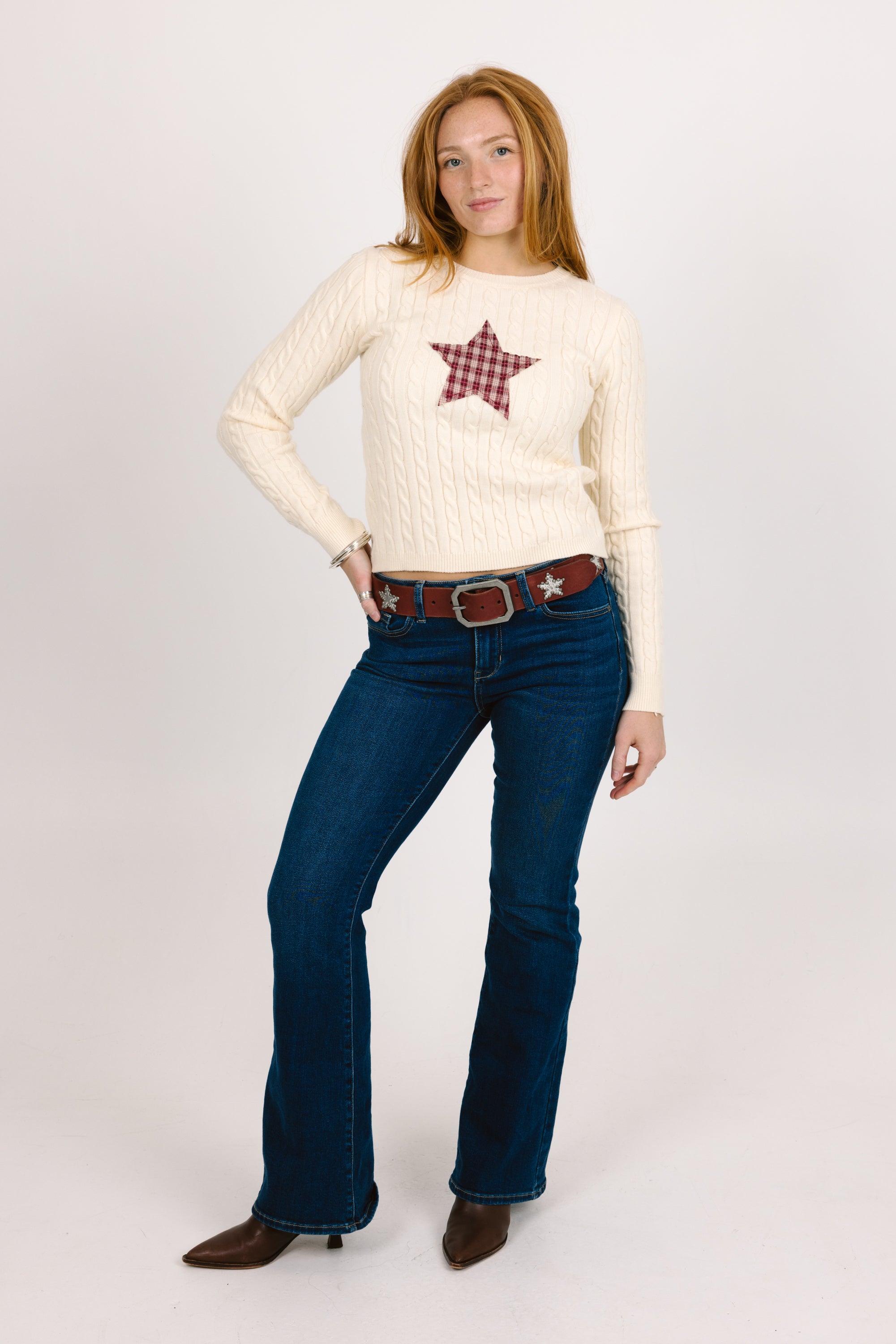 Woman wearing a cream sweater with a star design and blue jeans on a white background
