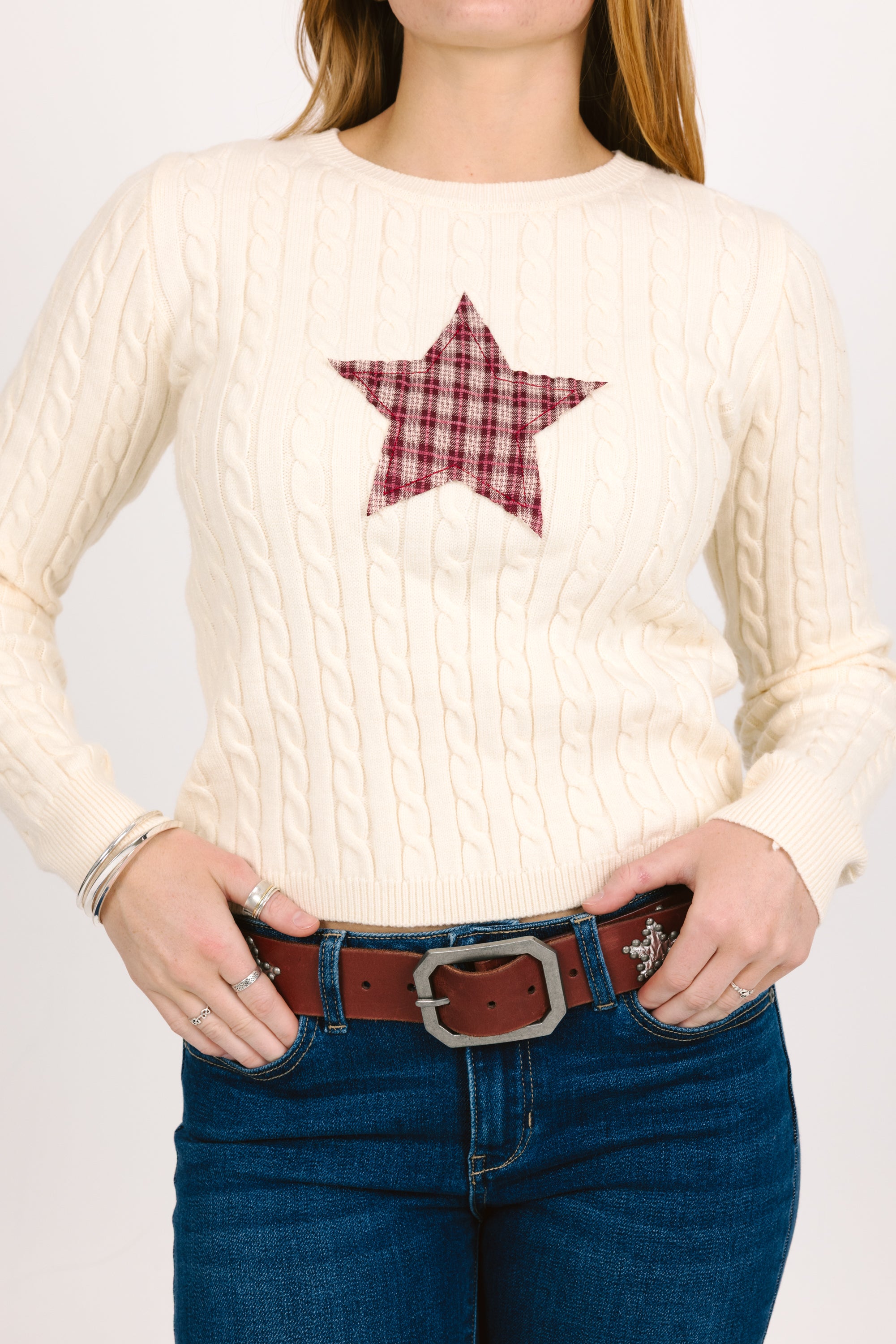 Person wearing a cream sweater with a red star patch and blue jeans.