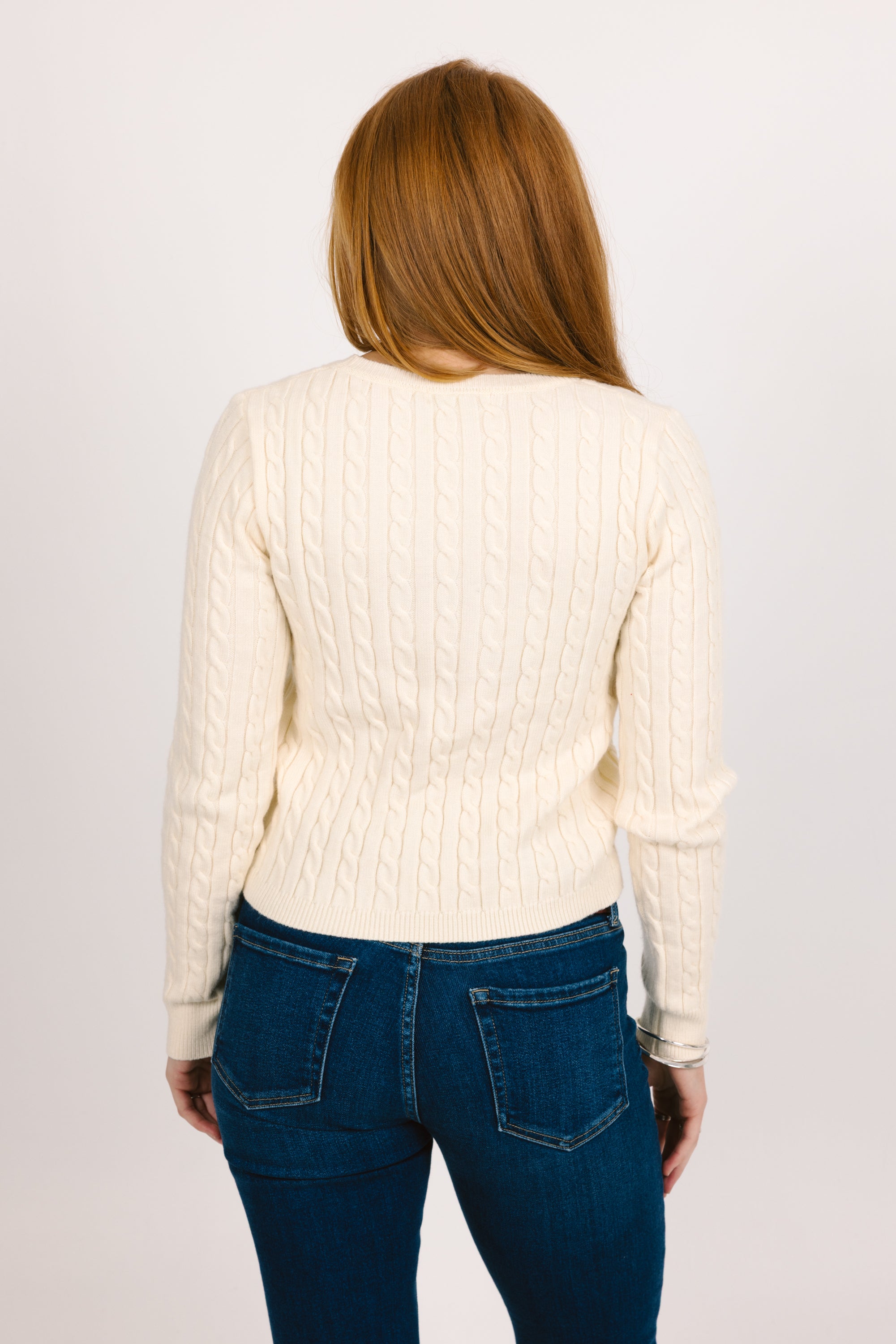 Person wearing a cream sweater and blue jeans on a plain background