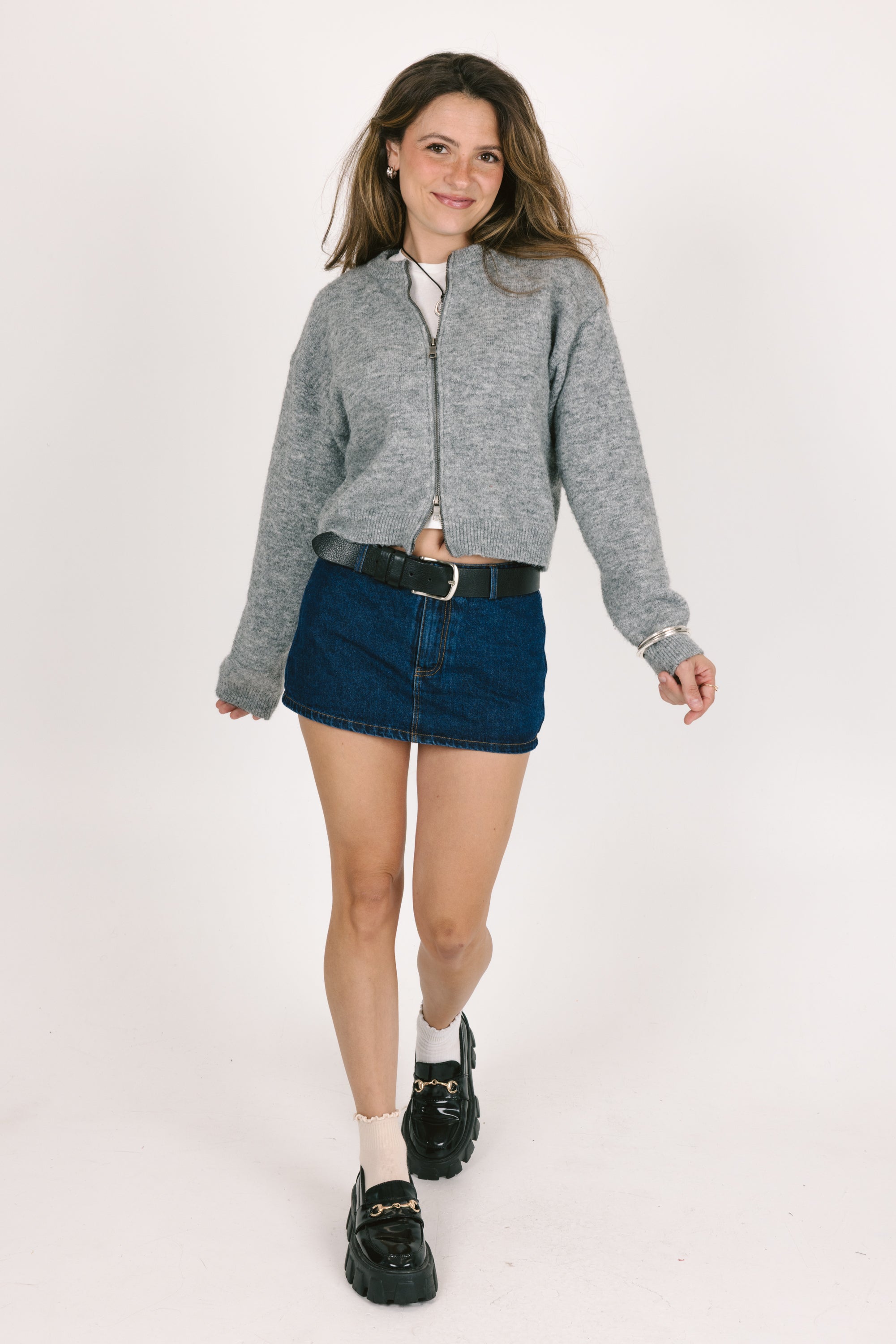 Woman wearing a gray jacket, blue denim skirt, and black shoes on a white background