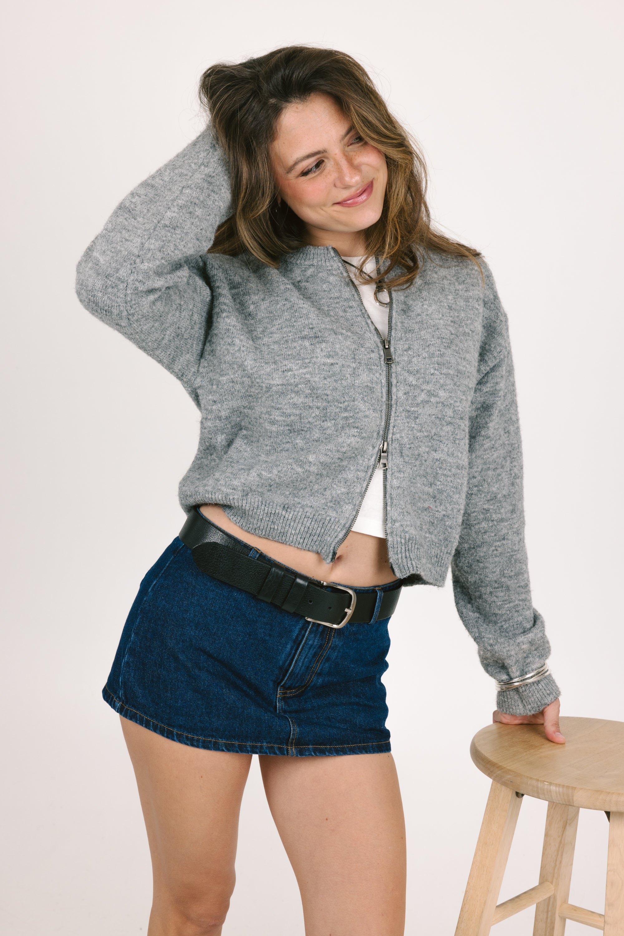 Woman wearing a gray cropped jacket and blue denim shorts on a white background