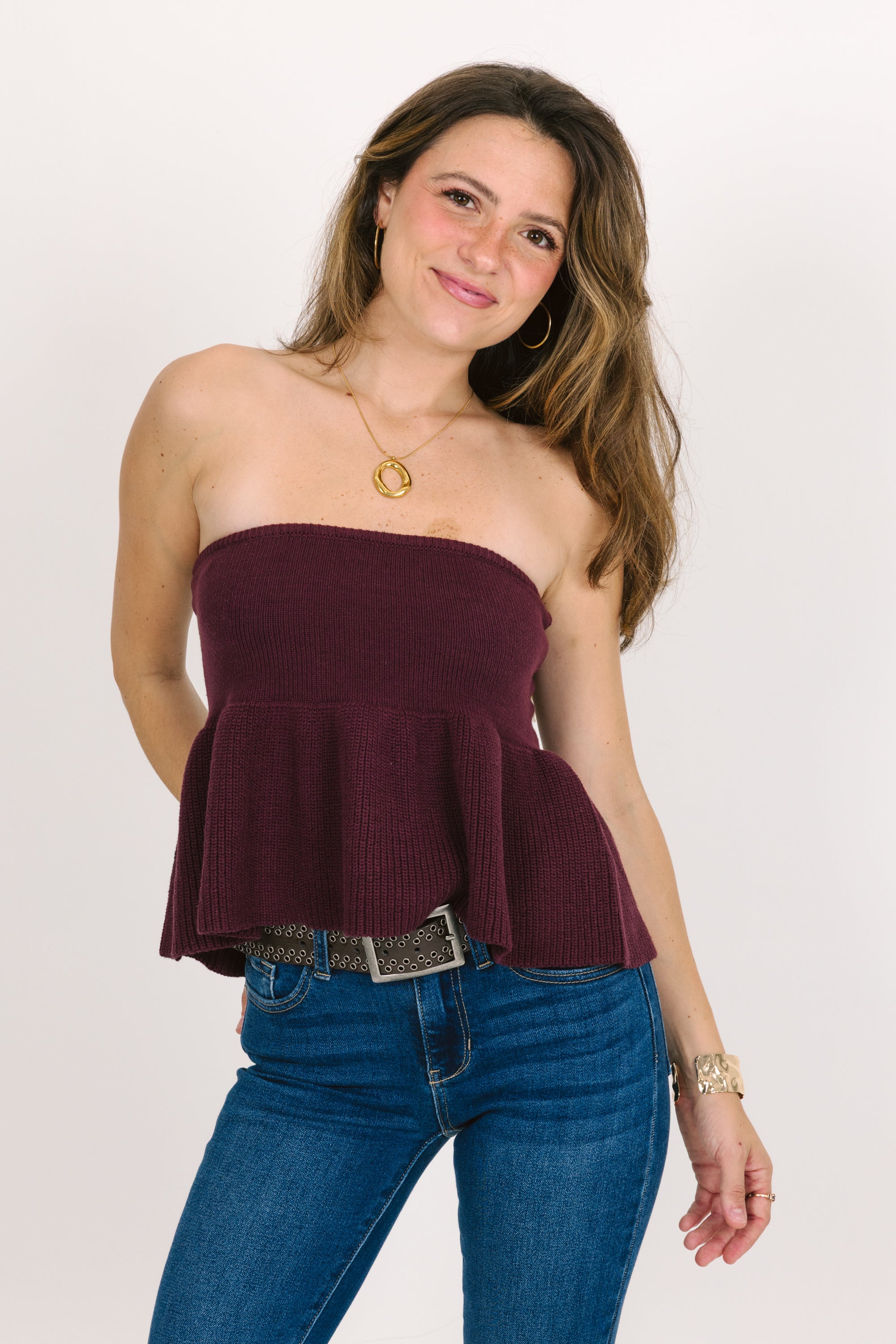 Woman wearing a strapless cranberry peplum top and blue jeans on a white background