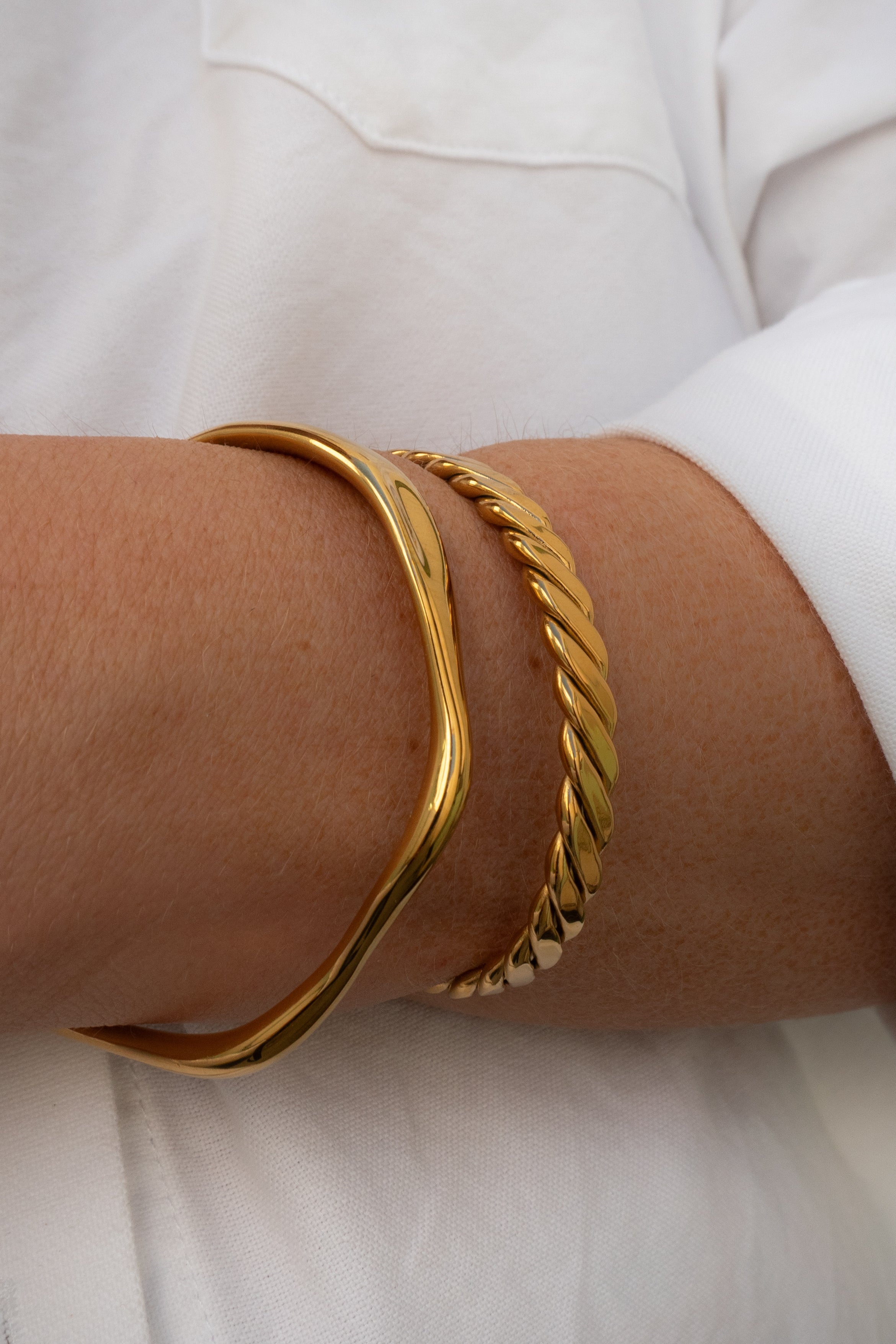 Gold bracelets on a person's wrist with a white background