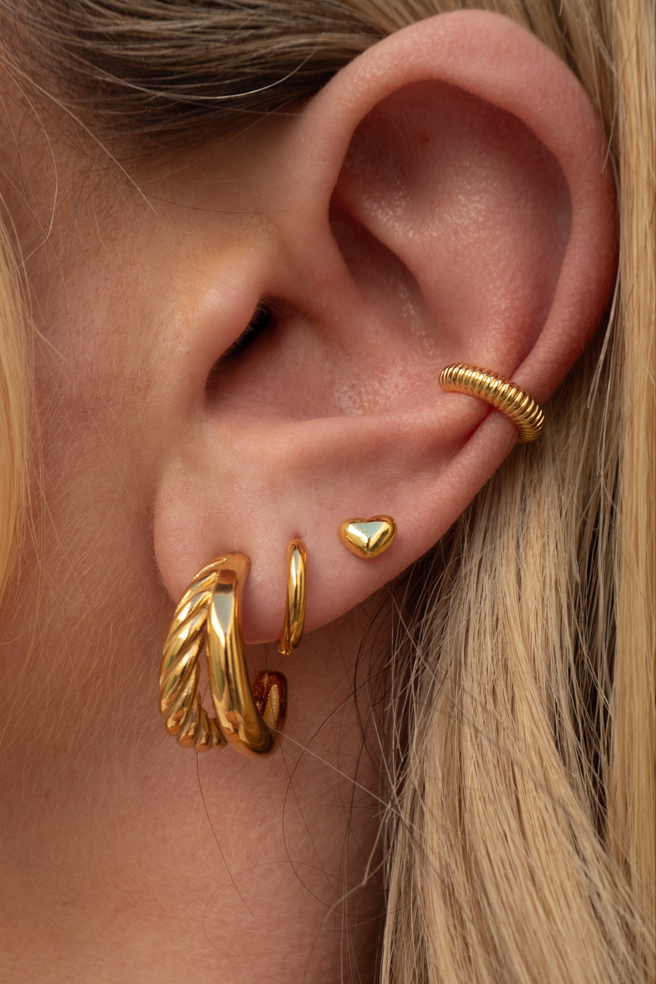 Close-up of an ear wearing gold hoop earrings and a heart-shaped stud.