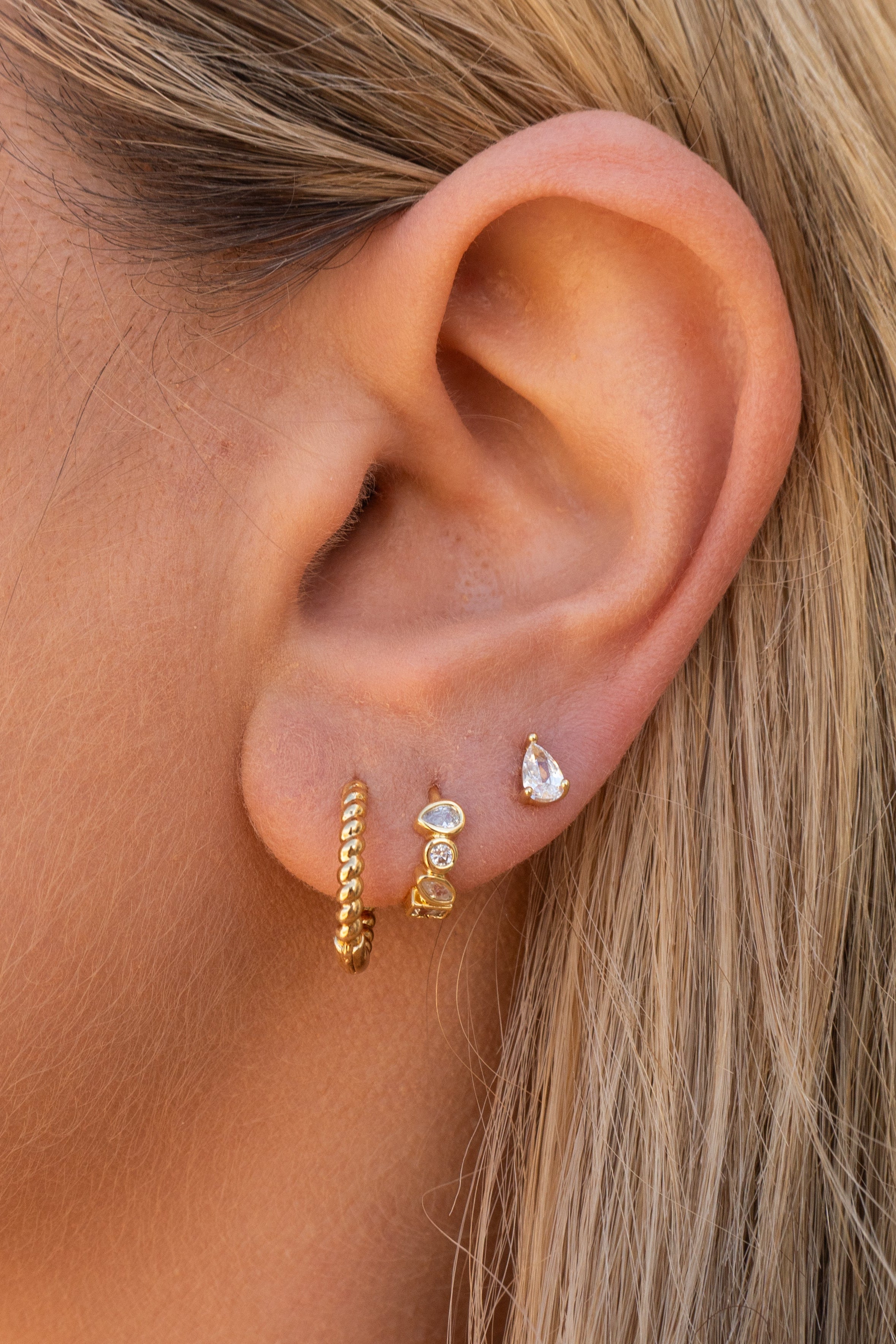 Close-up of an ear wearing gold hoop earrings with small gemstones.