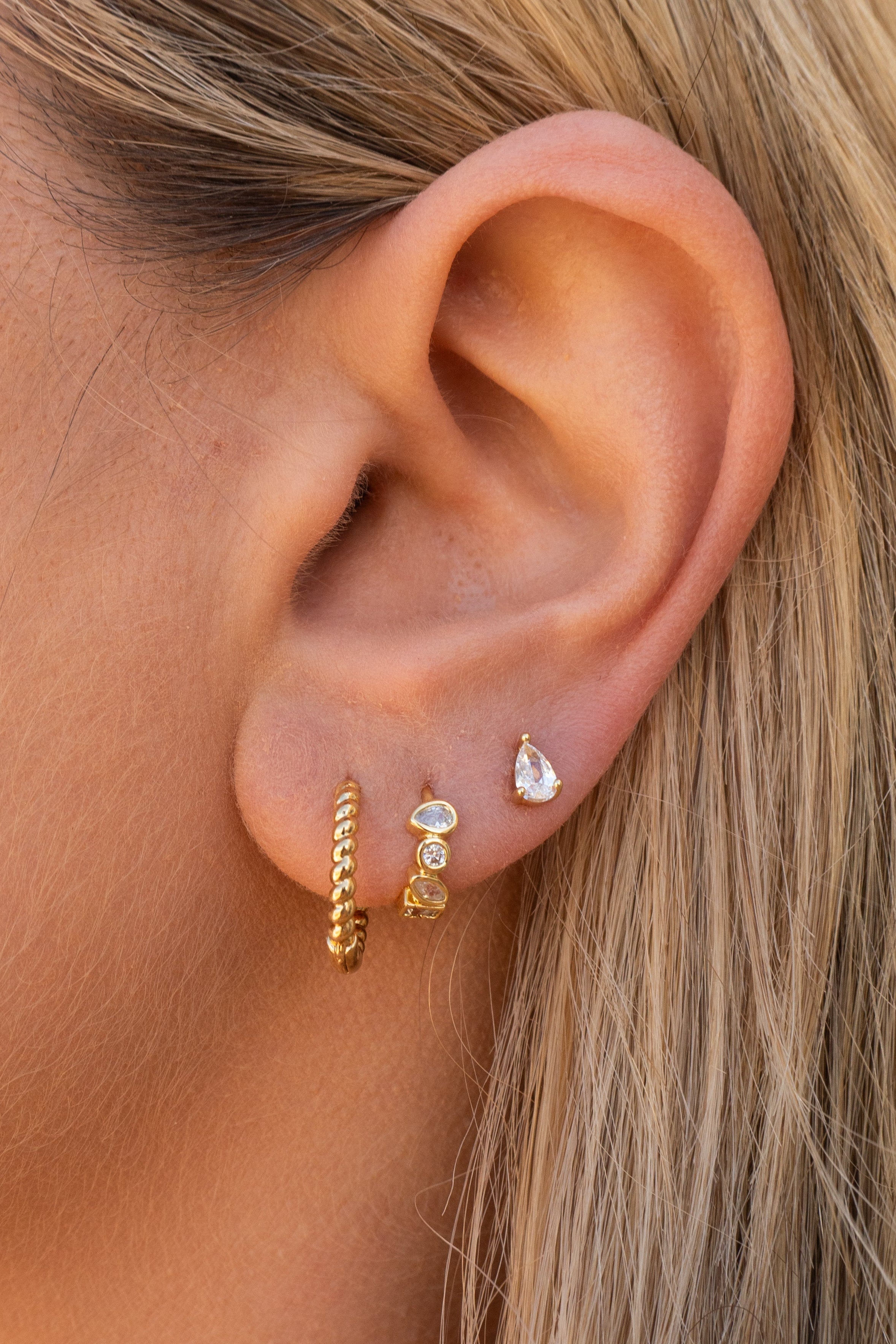 Close-up of an ear wearing gold hoop earrings with small gemstones.