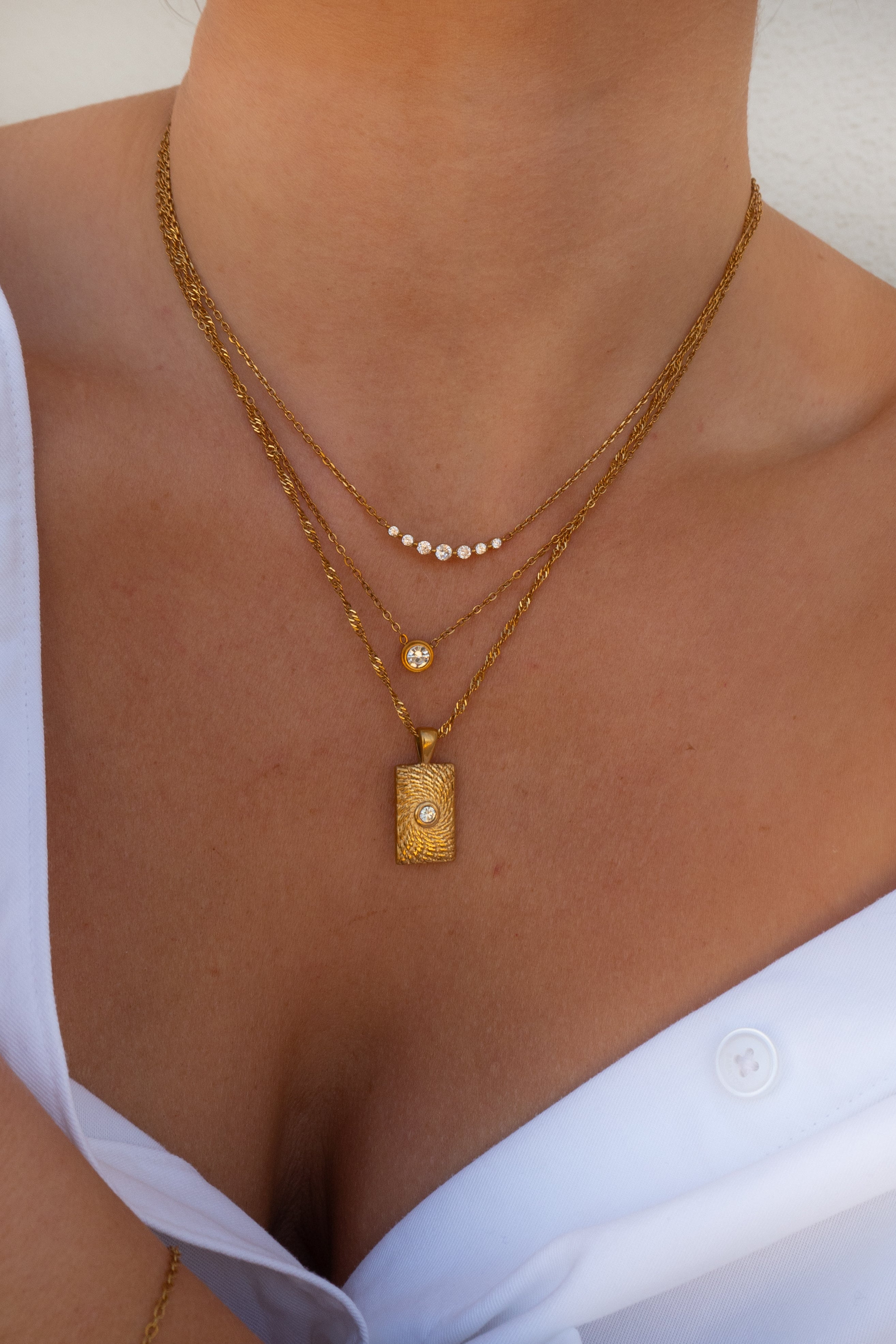 Close-up of a person wearing a gold necklace with a pendant on a plain background