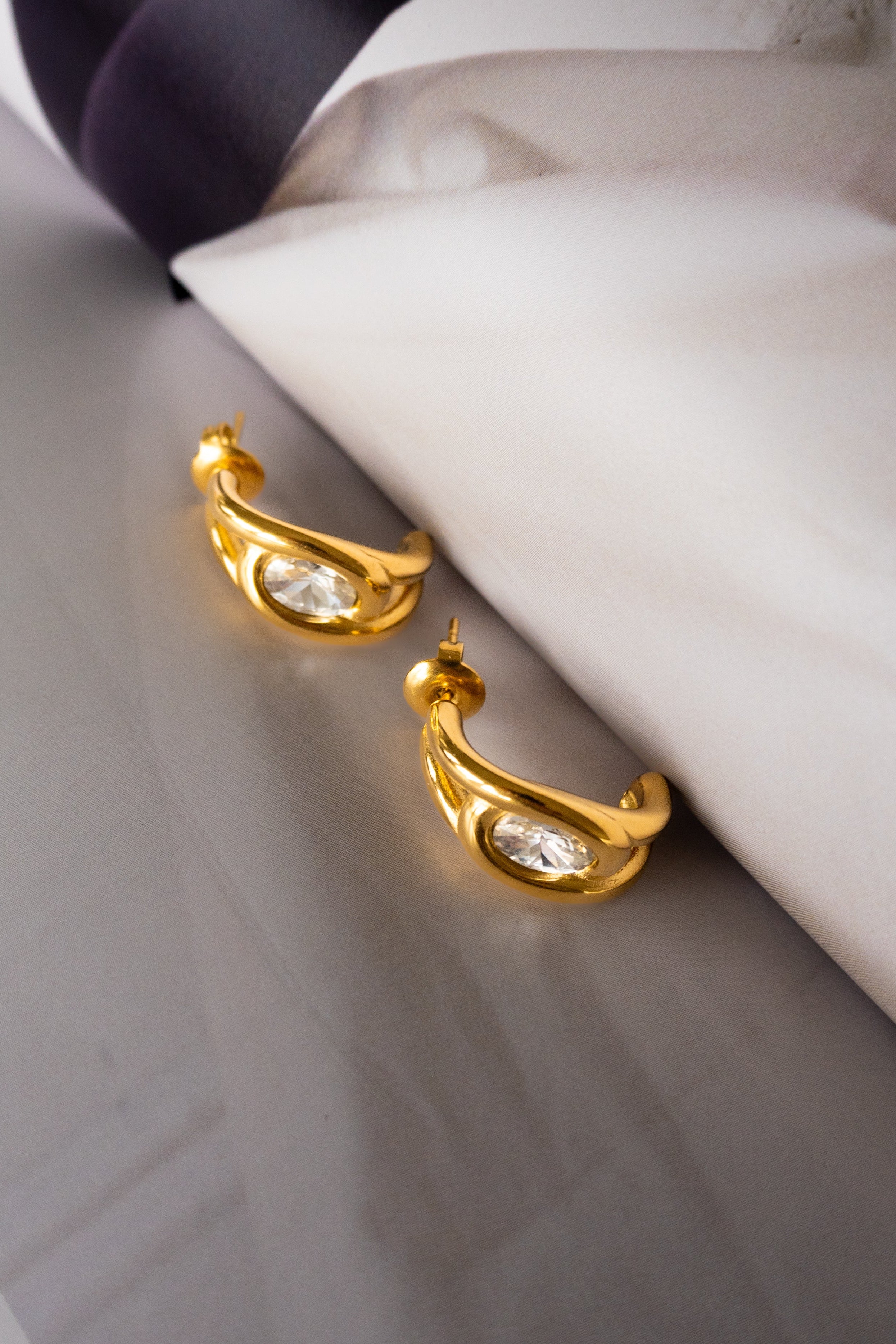 Gold earrings with clear stones on a marble surface